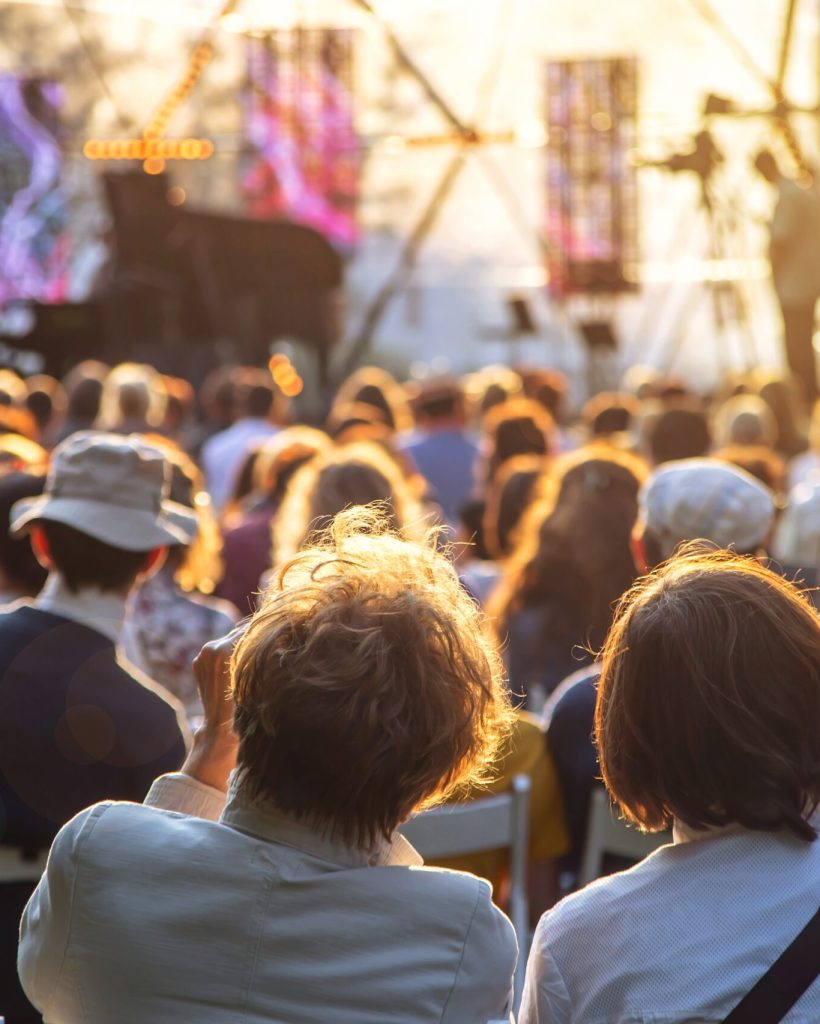 Cultural entertainment in the city in summer – openair concert Street concert in the park in summer backs of spectators sitting on chairs at the stage